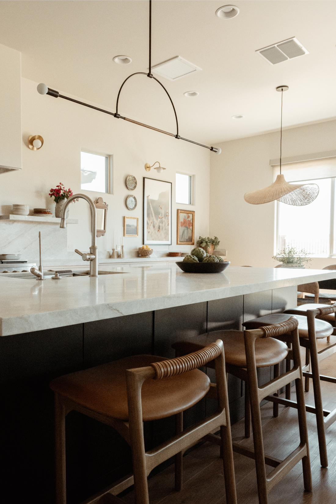 Warm modern kitchen at the Love & Recovery home, with marble island, woven pendant light, and a curated art wall