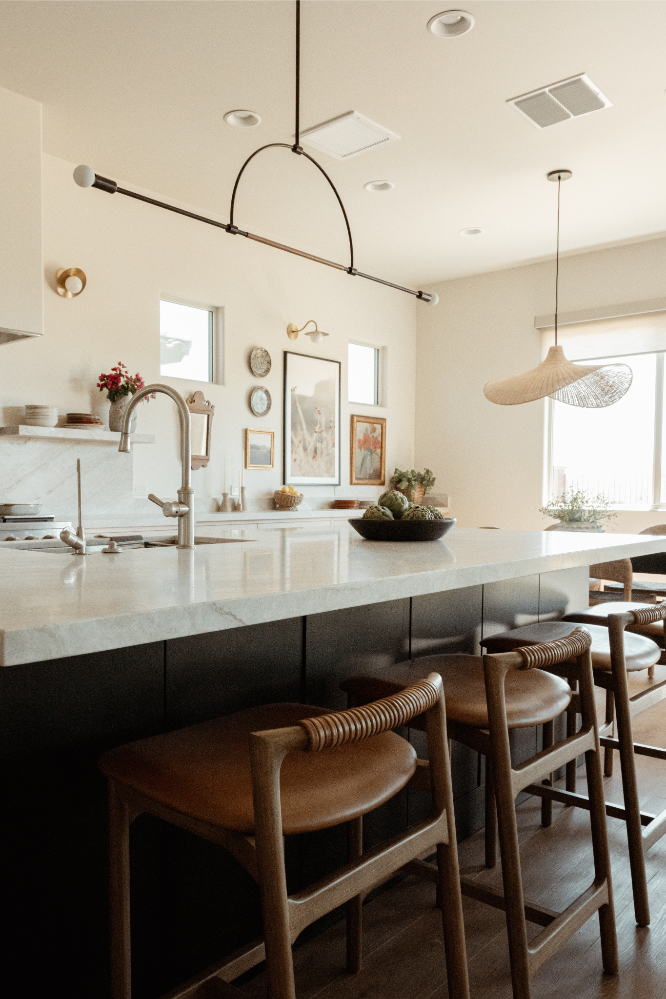 Warm modern kitchen at the Love & Recovery home, with marble island, woven pendant light, and a curated art wall