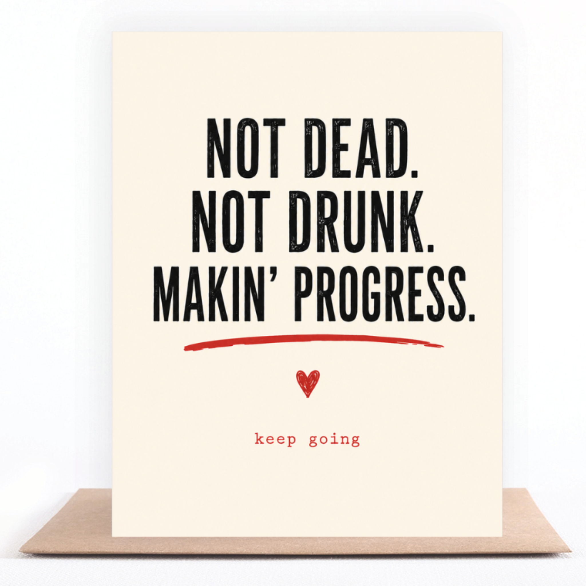Not Dead, Not Drunk, Keep Going greeting card standing on a kraft envelope