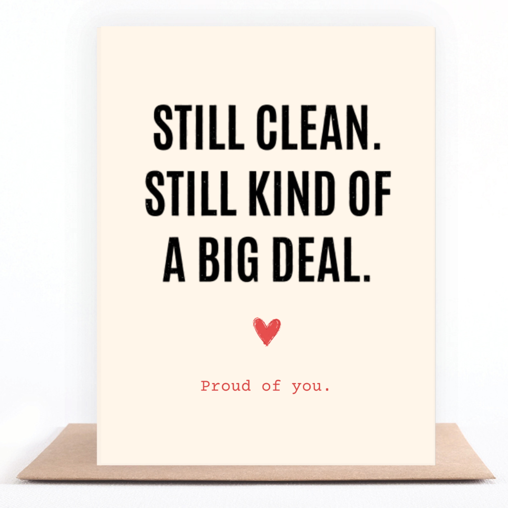 A cream-colored greeting card with bold black text reading 'STILL CLEAN. STILL KIND OF A BIG DEAL.