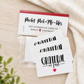 A set of white pocket affirmation cards in a clear plastic sleeve, with one card fanned out above the others. The top card has a red header and reads 'Pocket Pick-Me-Ups' with smaller text 'TINY AFFIRMATION CARDS TO SPREAD EVERYWHERE.