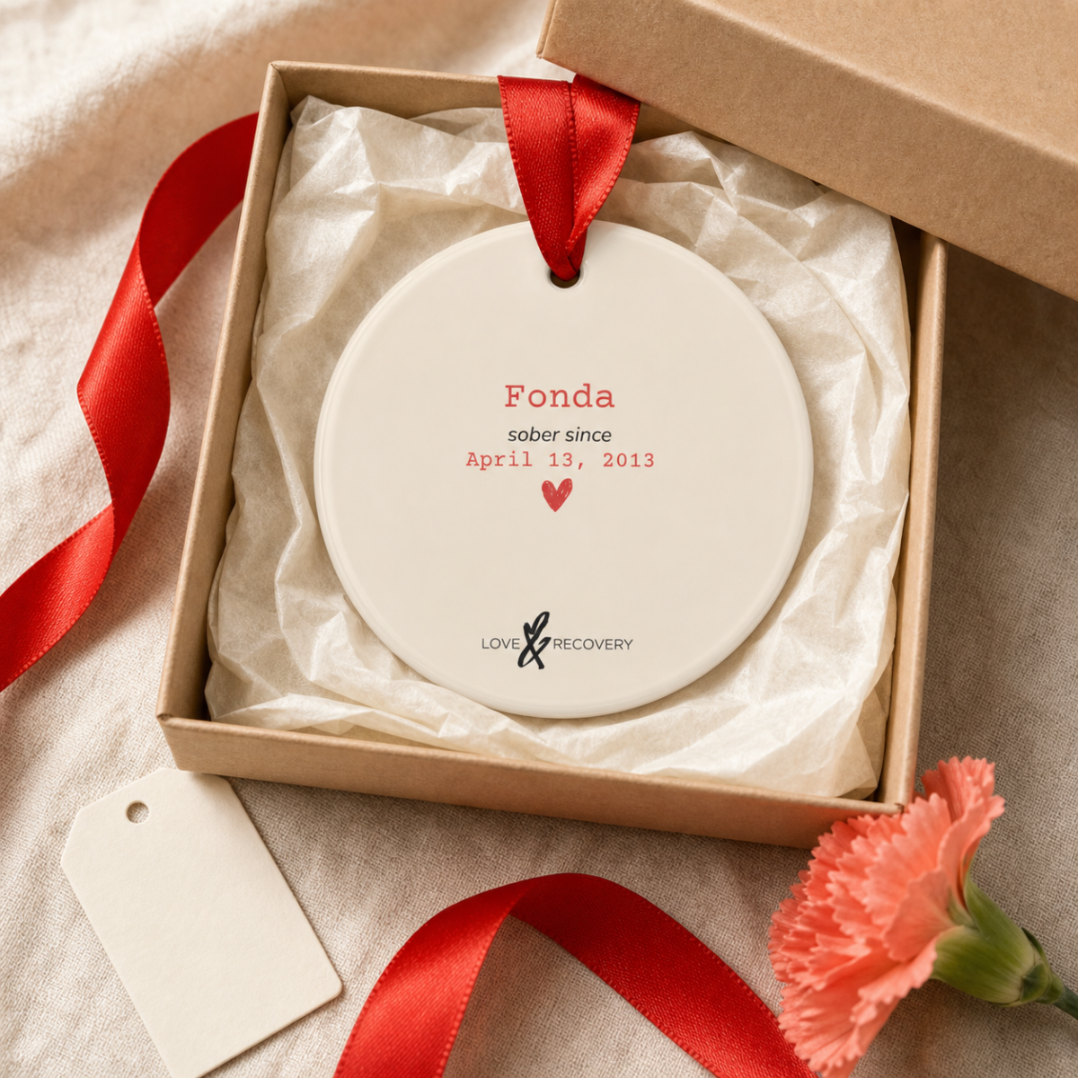 Personalized sobriety ornament nestled in a kraft gift box with tissue paper and red ribbon, ready to give