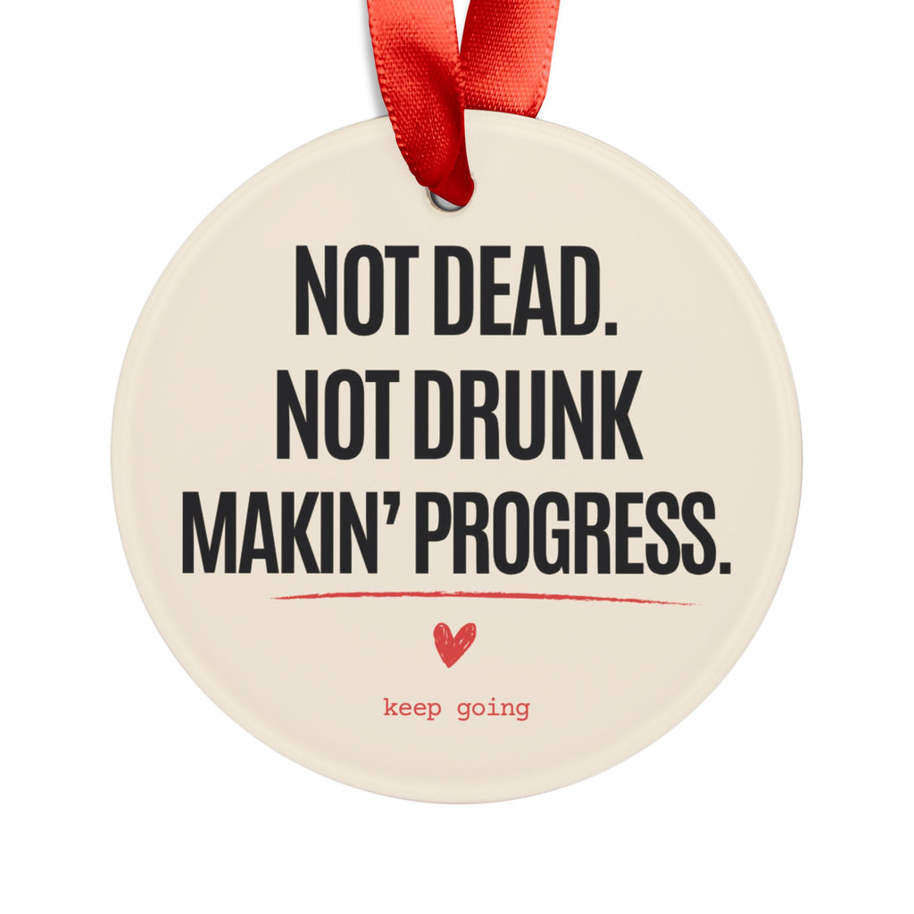 Personalized sobriety ornament reading Not Dead. Not Drunk. Makin' Progress. with a red ribbon, front view