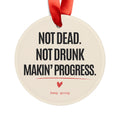 Personalized sobriety ornament reading Not Dead. Not Drunk. Makin' Progress. with a red ribbon, front view