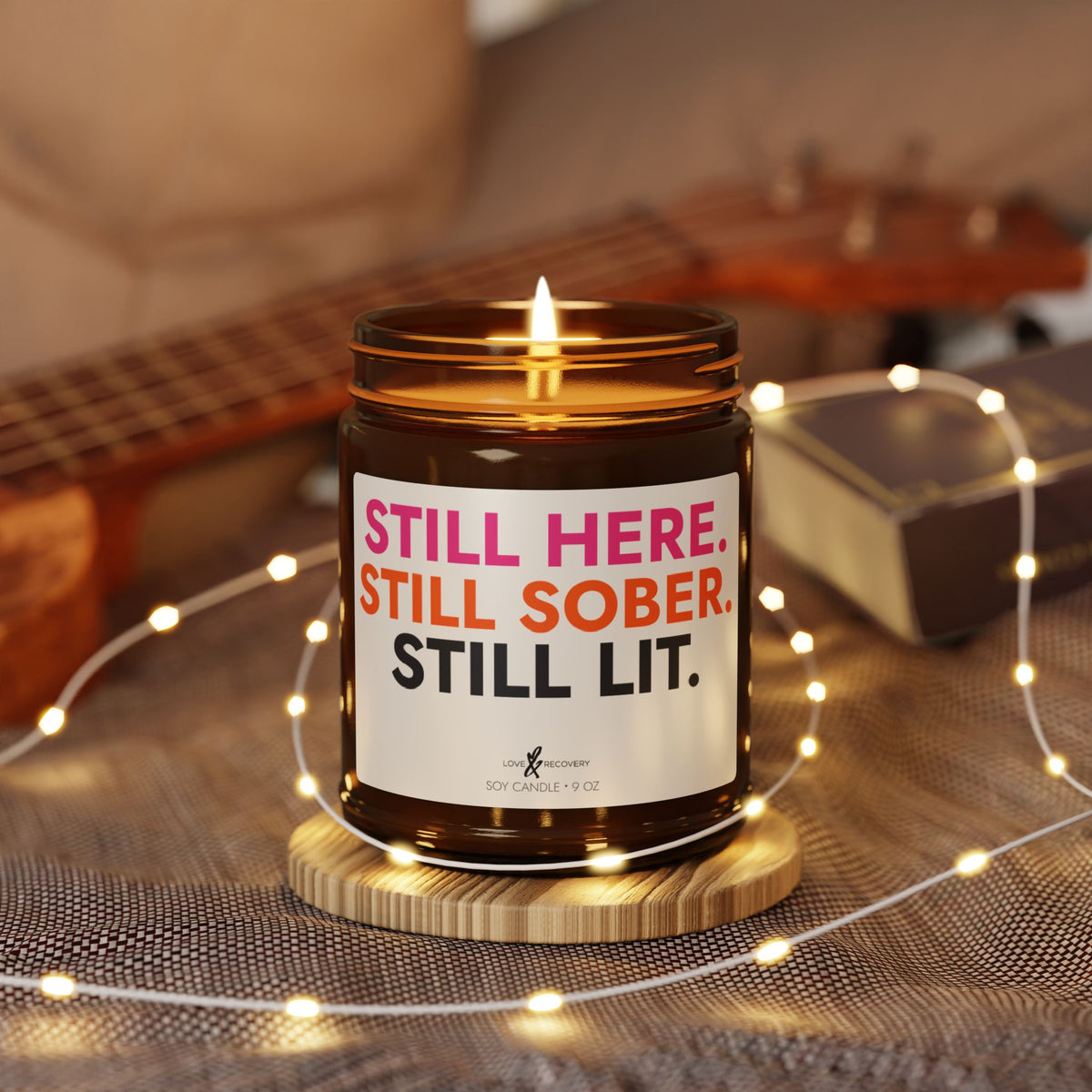 Lit sobriety candle in a 9 oz jar styled with string lights and a guitar for a cozy evening scene