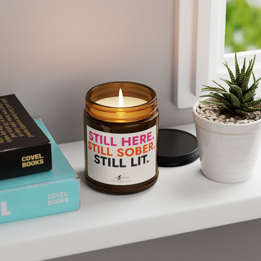 Lit sobriety candle in a 9 oz jar styled on a windowsill with books and a succulent